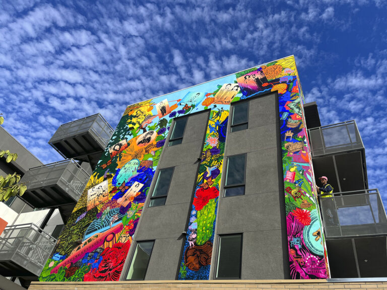 An image of a mural installed on a building featuring portraits of community members and cultural references.