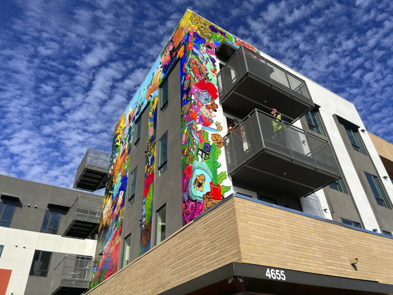 An image of a mural installed on a building featuring portraits of community members and cultural references.